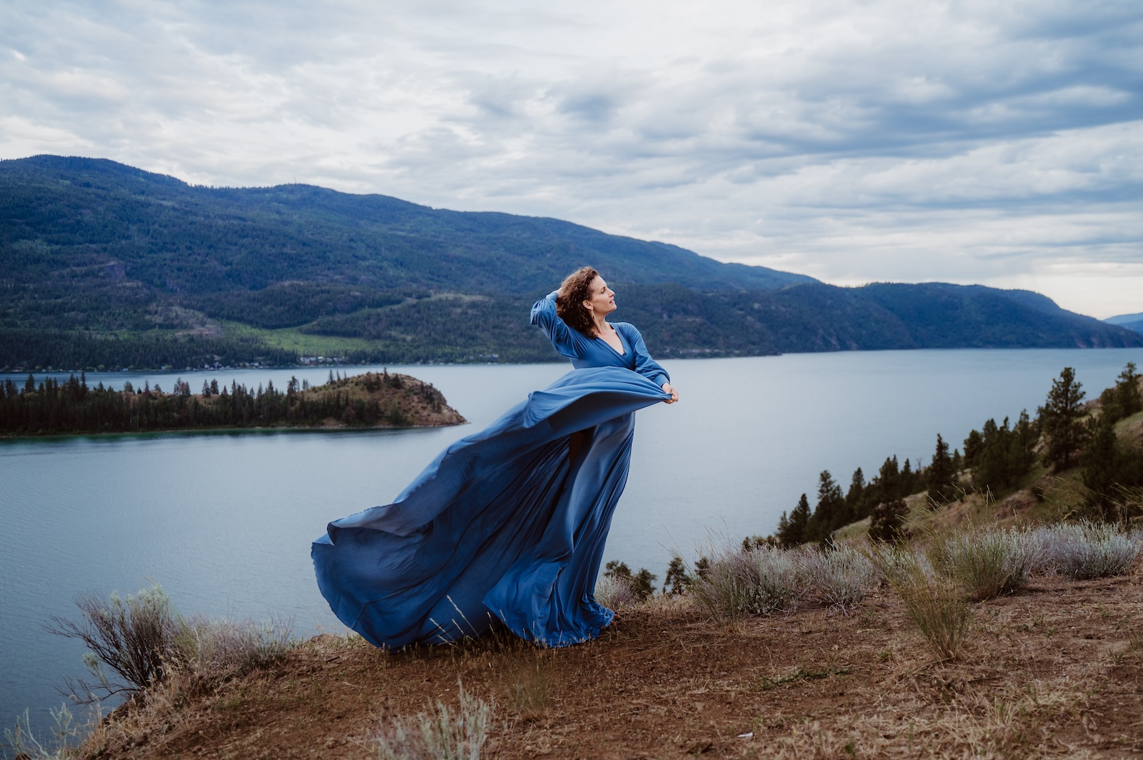 Rachel wyatt woman in blue dress blowing in the wind above kalamalka lake